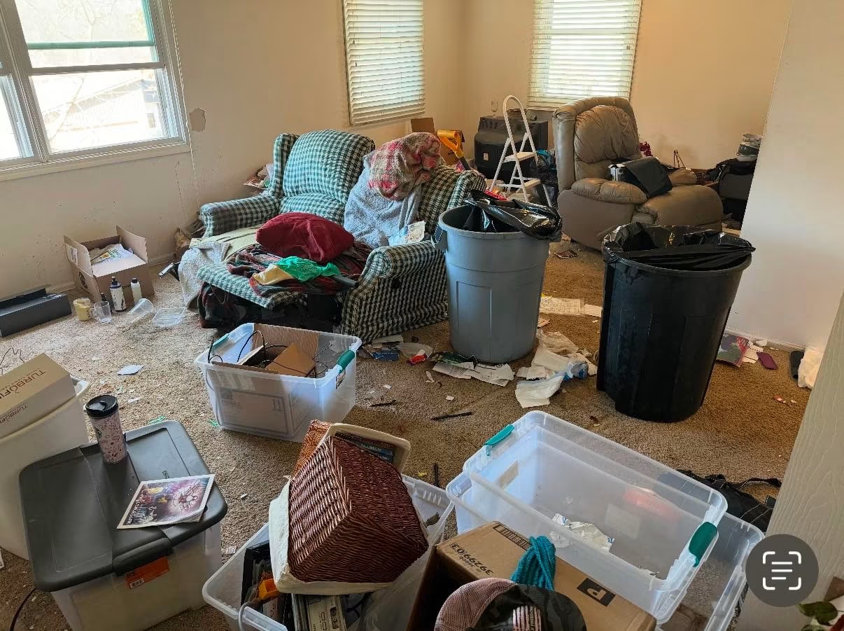 Living room before the clean-out — packed with furniture, totes, trash cans and clutter